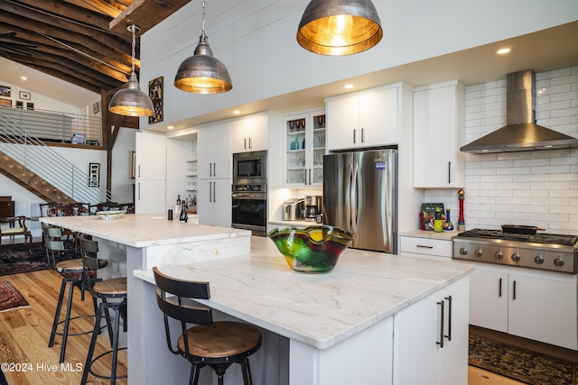 kitchen with wall chimney exhaust hood, a kitchen island, white cabinetry, and stainless steel appliances