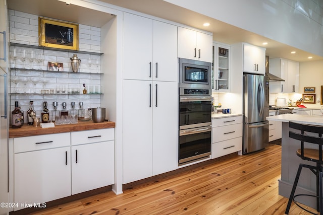 kitchen with wooden counters, appliances with stainless steel finishes, decorative backsplash, white cabinets, and light hardwood / wood-style floors