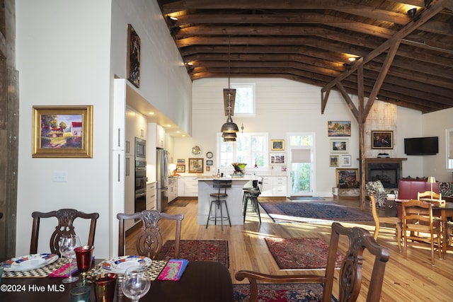 dining room featuring beam ceiling, a fireplace, high vaulted ceiling, and light wood-type flooring