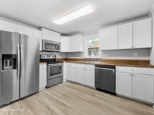 kitchen featuring appliances with stainless steel finishes, a textured ceiling, sink, light hardwood / wood-style flooring, and white cabinets