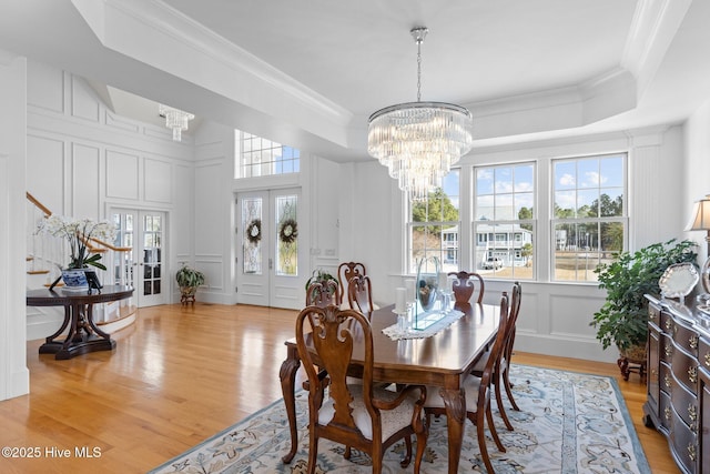 dining room with french doors, light hardwood / wood-style floors, a raised ceiling, a chandelier, and ornamental molding