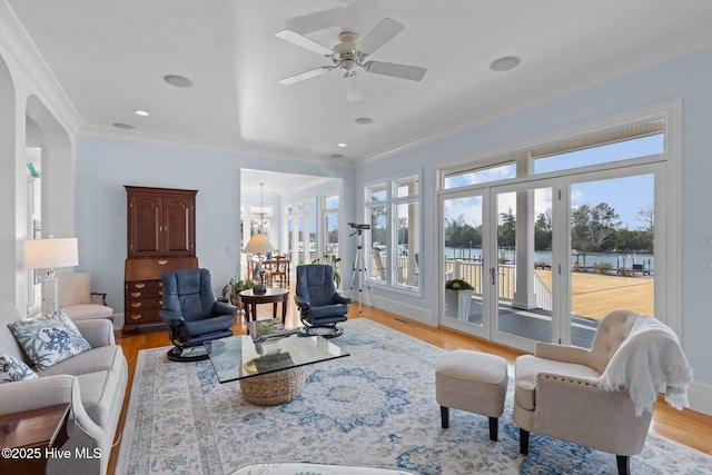 living room featuring ceiling fan with notable chandelier, crown molding, a water view, and light hardwood / wood-style flooring