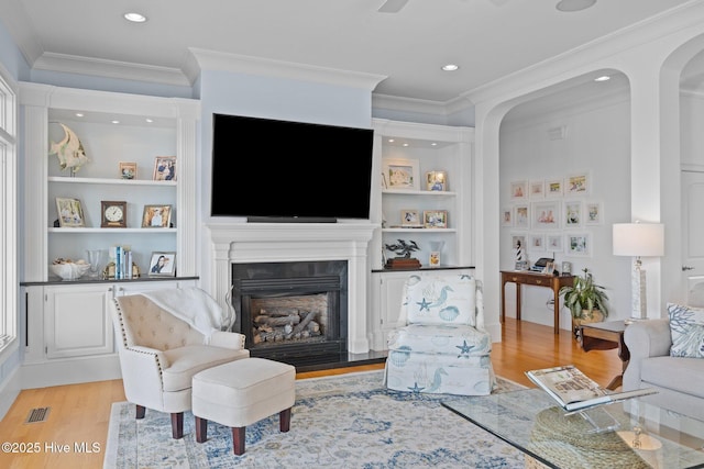 living room featuring built in shelves, light hardwood / wood-style flooring, and ornamental molding