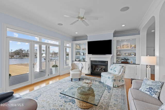 living room with ceiling fan, crown molding, a water view, and light hardwood / wood-style floors