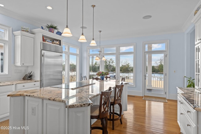 kitchen featuring built in refrigerator, a center island, decorative light fixtures, white cabinetry, and a healthy amount of sunlight