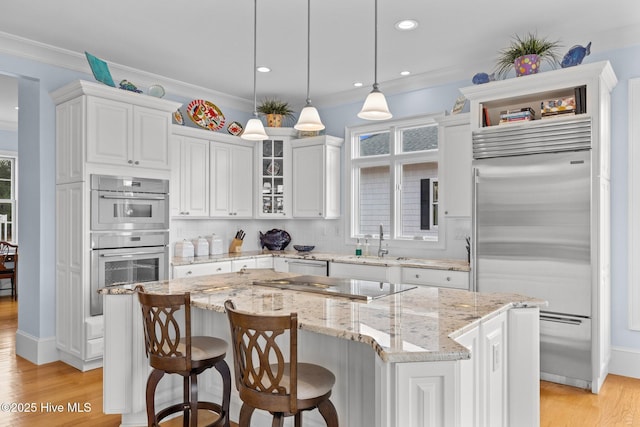 kitchen with white cabinets, appliances with stainless steel finishes, a kitchen island, hanging light fixtures, and light stone counters