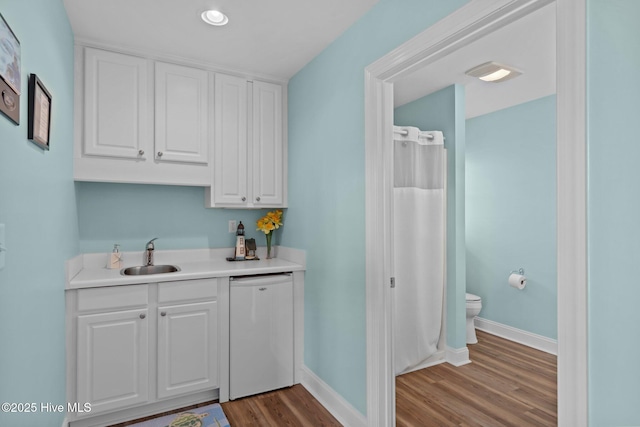 bar featuring white dishwasher, sink, white cabinetry, and dark hardwood / wood-style flooring