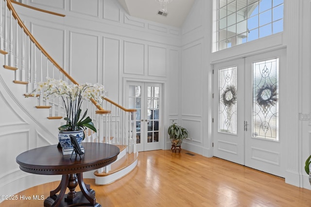 foyer entrance with light wood-type flooring, french doors, and a towering ceiling