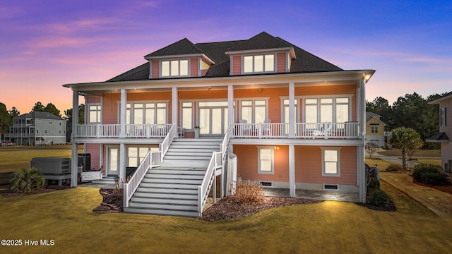 back house at dusk featuring a lawn, cooling unit, a hot tub, and a porch