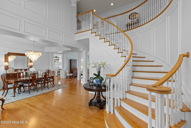 stairway featuring a high ceiling, hardwood / wood-style floors, a notable chandelier, decorative columns, and crown molding