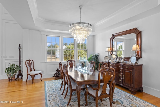 dining area with light hardwood / wood-style floors, crown molding, a raised ceiling, and a chandelier