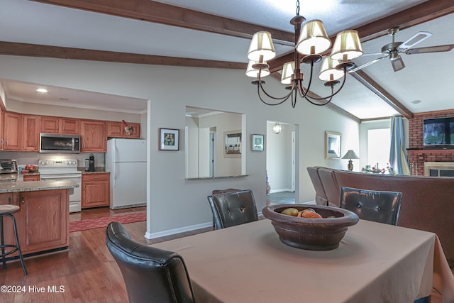 dining area with dark hardwood / wood-style flooring, lofted ceiling with beams, ceiling fan with notable chandelier, and a brick fireplace