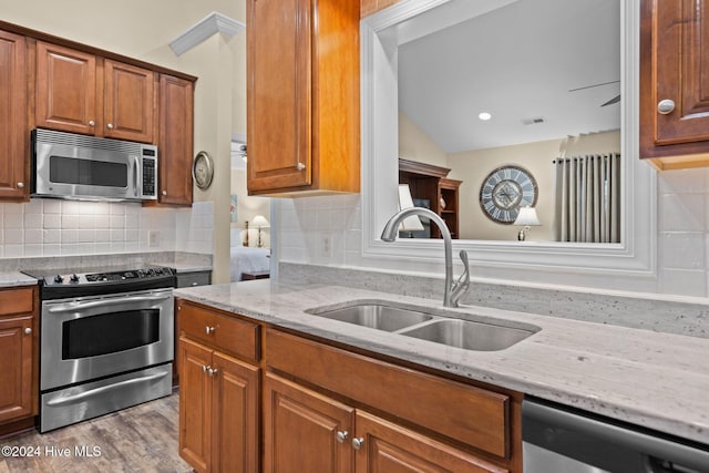 kitchen featuring backsplash, light stone counters, sink, and appliances with stainless steel finishes