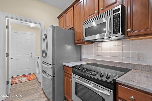 kitchen featuring appliances with stainless steel finishes, backsplash, light stone counters, washing machine and dryer, and light hardwood / wood-style floors