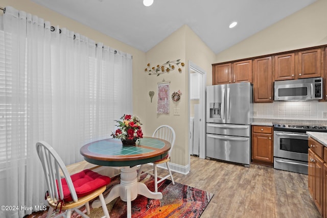 kitchen featuring decorative backsplash, light hardwood / wood-style floors, vaulted ceiling, and appliances with stainless steel finishes