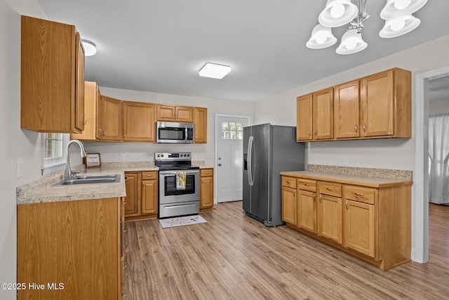 kitchen with sink, appliances with stainless steel finishes, light hardwood / wood-style flooring, and a notable chandelier