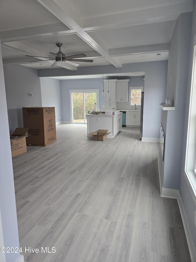 unfurnished living room featuring light wood-type flooring, coffered ceiling, ceiling fan, sink, and beam ceiling