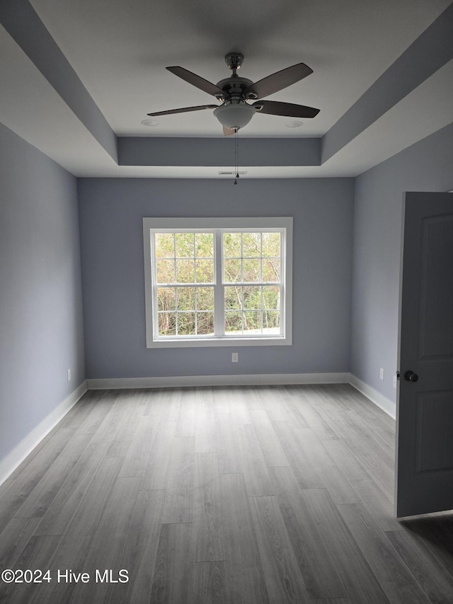 unfurnished room with a raised ceiling, light hardwood / wood-style flooring, and ceiling fan