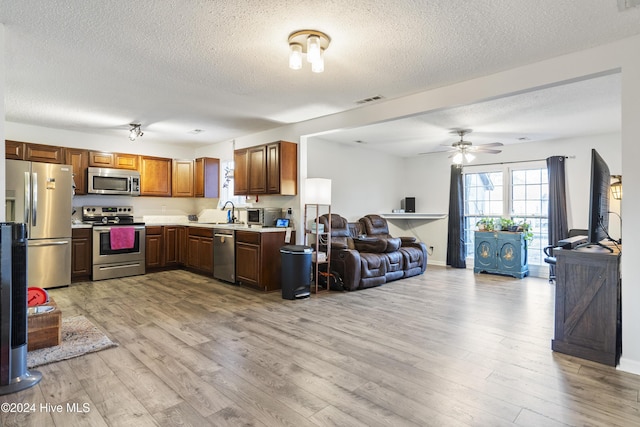 kitchen with a textured ceiling, ceiling fan, stainless steel appliances, and light hardwood / wood-style flooring