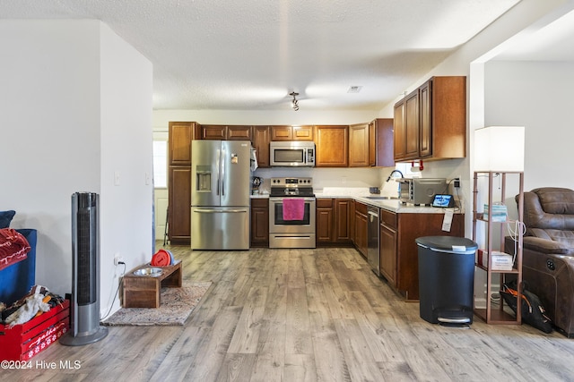 kitchen with appliances with stainless steel finishes, light wood-type flooring, a textured ceiling, and sink