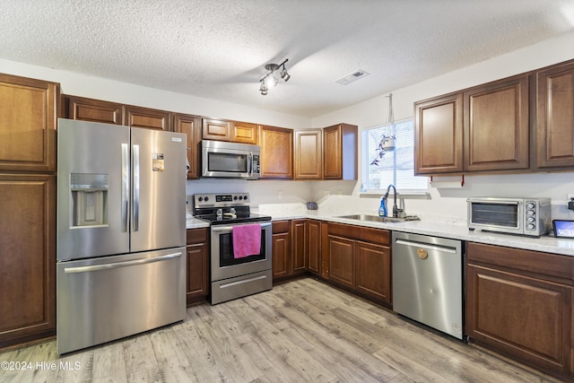 kitchen featuring a textured ceiling, sink, light wood-type flooring, and stainless steel appliances