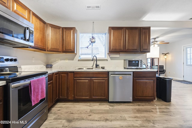 kitchen with ceiling fan, sink, hanging light fixtures, appliances with stainless steel finishes, and light wood-type flooring