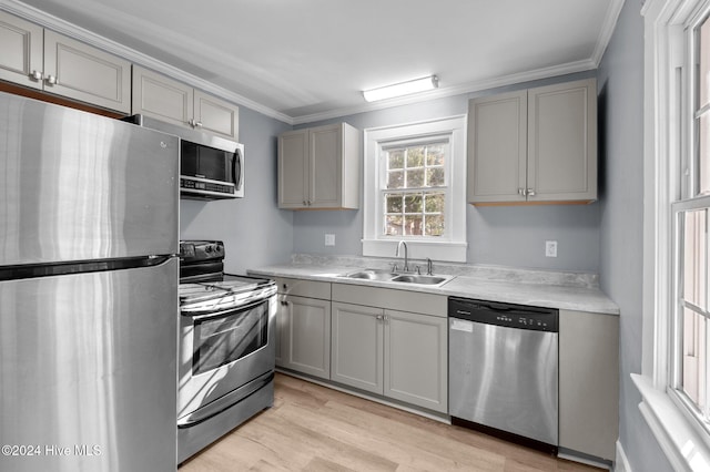 kitchen featuring stainless steel appliances, crown molding, light hardwood / wood-style floors, and sink