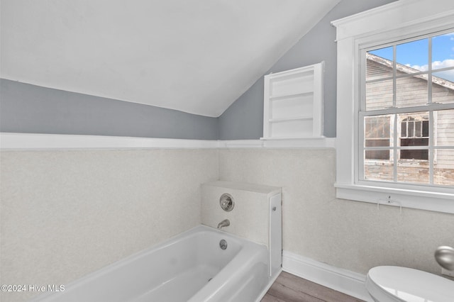 bathroom with toilet, hardwood / wood-style floors, a tub to relax in, and vaulted ceiling