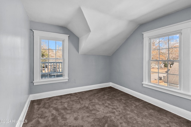 bonus room featuring a healthy amount of sunlight, vaulted ceiling, and dark carpet