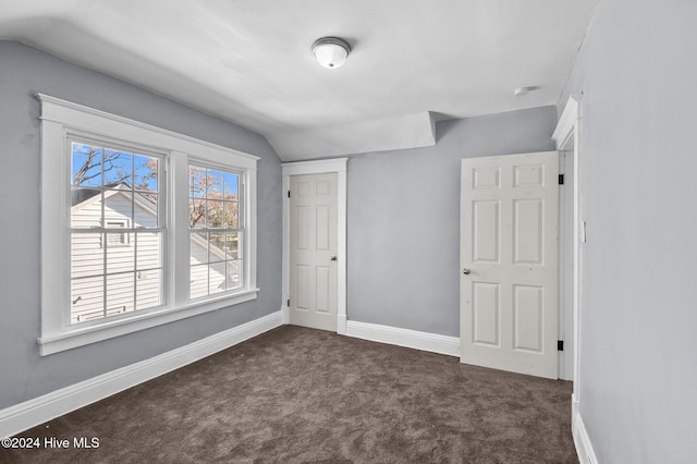 unfurnished bedroom with a closet, lofted ceiling, and dark colored carpet