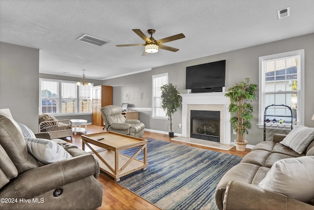 living room with ceiling fan with notable chandelier, wood-type flooring, a textured ceiling, and plenty of natural light