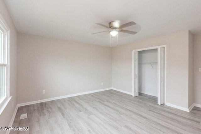 unfurnished bedroom featuring multiple windows, ceiling fan, a closet, and light wood-type flooring