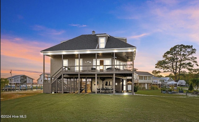 back house at dusk featuring a lawn, a patio, and a wooden deck