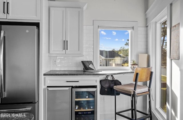 interior space featuring a healthy amount of sunlight, white cabinetry, stainless steel refrigerator, and dark stone counters