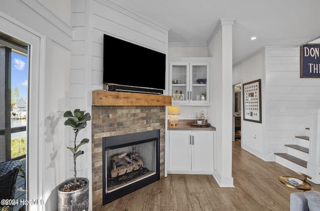 bar with white cabinetry, a fireplace, ornamental molding, and hardwood / wood-style flooring