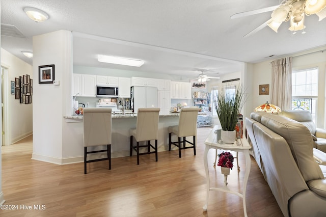 kitchen featuring light stone counters, a breakfast bar, white refrigerator, white cabinets, and light hardwood / wood-style floors