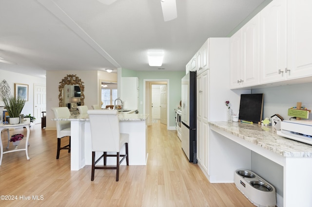 kitchen featuring a breakfast bar, kitchen peninsula, white cabinets, and light hardwood / wood-style floors