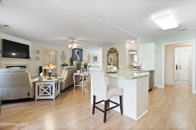 kitchen featuring sink, stainless steel dishwasher, ceiling fan, light wood-type flooring, and a breakfast bar area