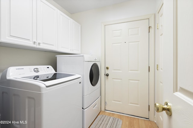 laundry area featuring washing machine and clothes dryer, cabinets, and light hardwood / wood-style floors