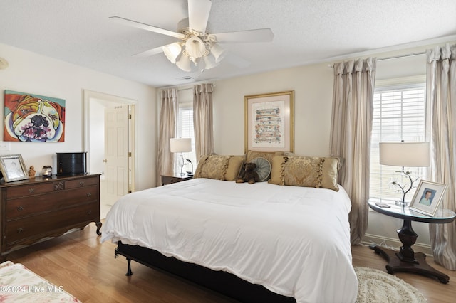 bedroom with a textured ceiling, ceiling fan, light hardwood / wood-style flooring, and multiple windows