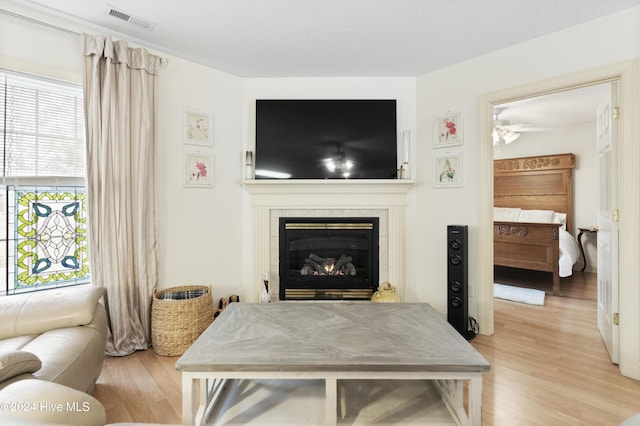 living room featuring ceiling fan, a healthy amount of sunlight, a tile fireplace, and light hardwood / wood-style flooring