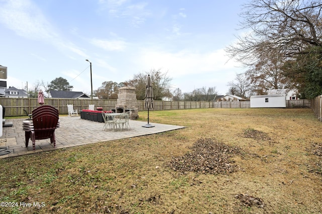 view of yard with an outdoor stone fireplace, a storage shed, and a patio