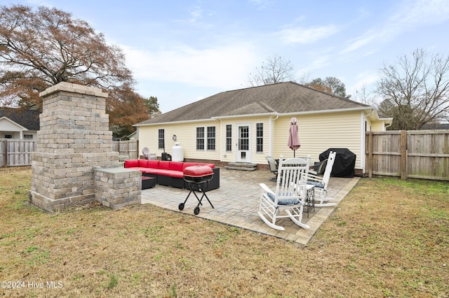 rear view of property featuring a lawn, an outdoor living space with a fireplace, and a patio