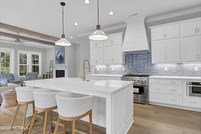 kitchen with a kitchen island with sink, white cabinets, appliances with stainless steel finishes, beamed ceiling, and custom range hood