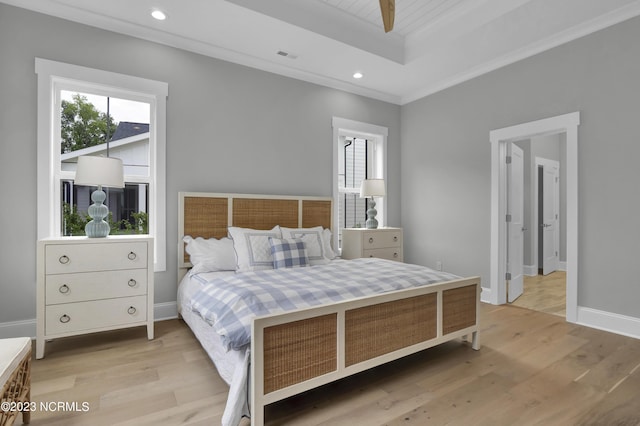 bedroom featuring light hardwood / wood-style floors, ornamental molding, and a tray ceiling