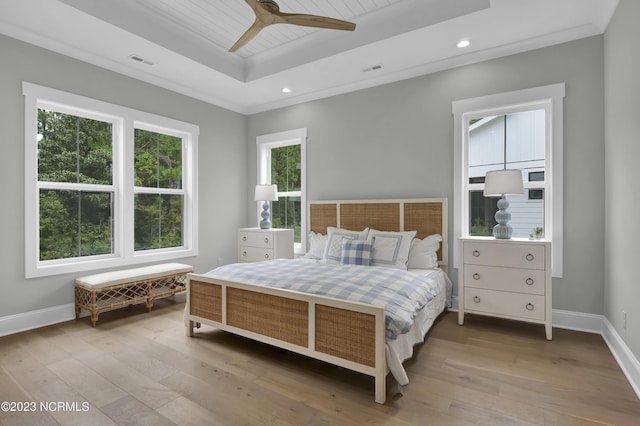 bedroom with ornamental molding, light hardwood / wood-style floors, ceiling fan, and a tray ceiling