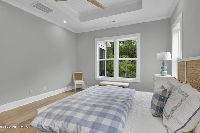 bedroom featuring ceiling fan, crown molding, light hardwood / wood-style flooring, and a tray ceiling