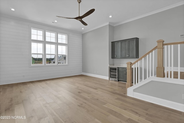 unfurnished living room with wine cooler, wooden walls, light hardwood / wood-style flooring, and ornamental molding