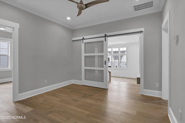 unfurnished room featuring hardwood / wood-style flooring, ceiling fan, and a barn door