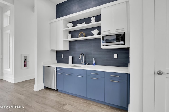 kitchen with stainless steel appliances, blue cabinets, sink, white cabinets, and light hardwood / wood-style floors